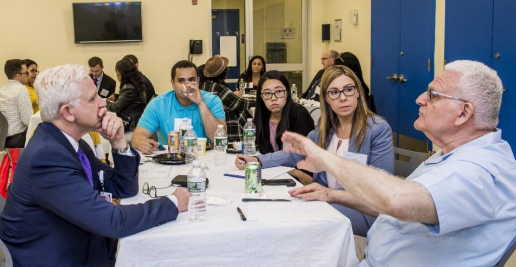 This photo shows community members sitting at a round table during an event.