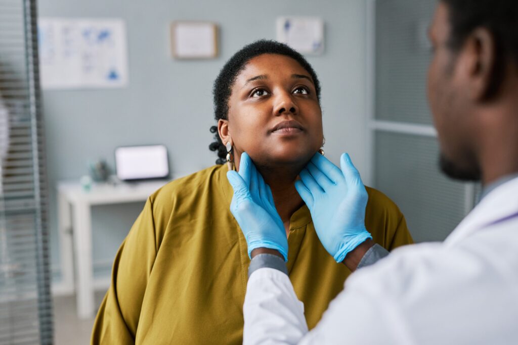 This photo shows a black woman at a health checkup with a doctor who is examining her neck.